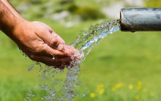 A person holds out their hands under running water, demonstrating a potable water tank.