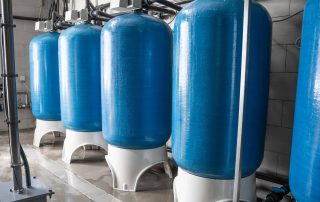 Five blue potable water tanks are displayed on a concrete floor.