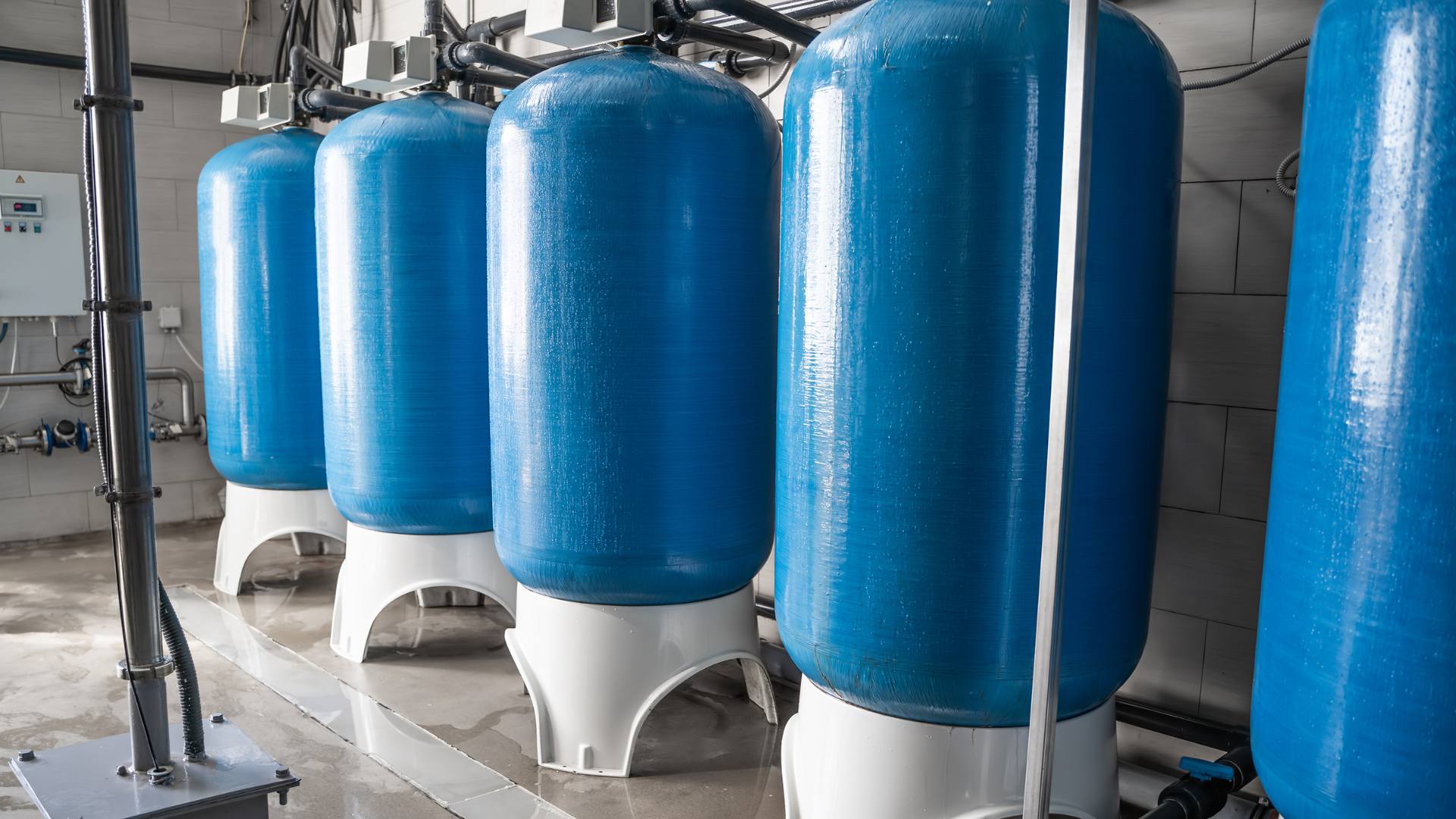 Five blue potable water tanks are displayed on a concrete floor.